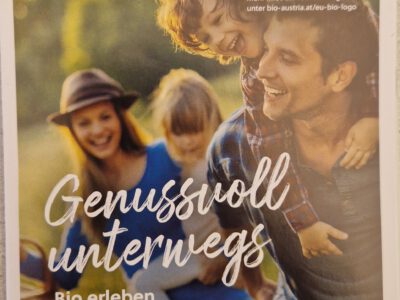 Titelbild_Genussvoll wandern Mann trägt Kind, huckepack dahinter lachende Frau mit Hut und Mädchen am Arm