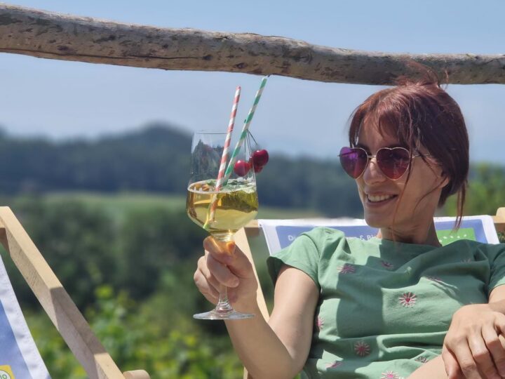 Dunkelhaarige Frau mit Sonnenbrille und Weinglas sitzt am Liegestuhl